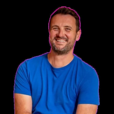 Man with dark hair and beard wearing bright blue t-shirt, smiling at camera against dark background
